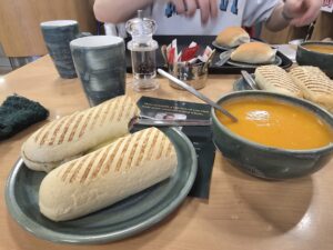 A halved panini on a plate, next to a bowl of orange soup in a cafe.