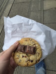 A hand holding a cookie with a chocolate bar in the centre of it.