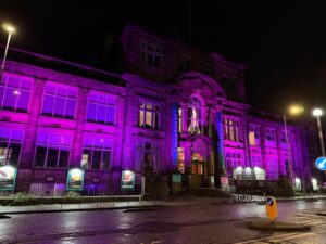 Exterior of Summerhall, at night, lit up with purple lights.