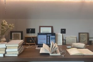 A laptop, and open book and additional piles of books on a desk.