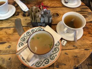 A large cup of soup and a a cup of tea on a table in a cafe.