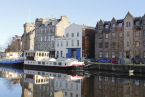 A boat on the water at The Shore in Leith, Edinburgh. The boat is moored in front of a variety buildings that line the street.