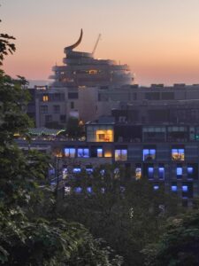 Sun sets behind St James Quarter and surrounding buildings in Edinburgh. A large architectural spiral is a prominent feature in the skyline. 