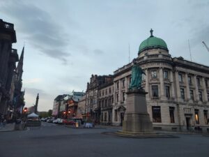 Exteriors of the buildings lining a portion of George Street in Edinburgh, with a sculpture in the foreground,