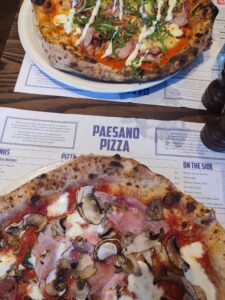 Two pizzas on a table with a Paesano Pizza menu underneath them. 