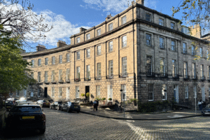A street in Stockbridge, Edinburgh, with people walking on the pavement and cars parked on the side of the road.
