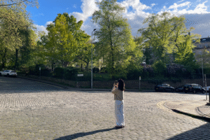 A person taking a photograph, blue skies and greenery in the background.