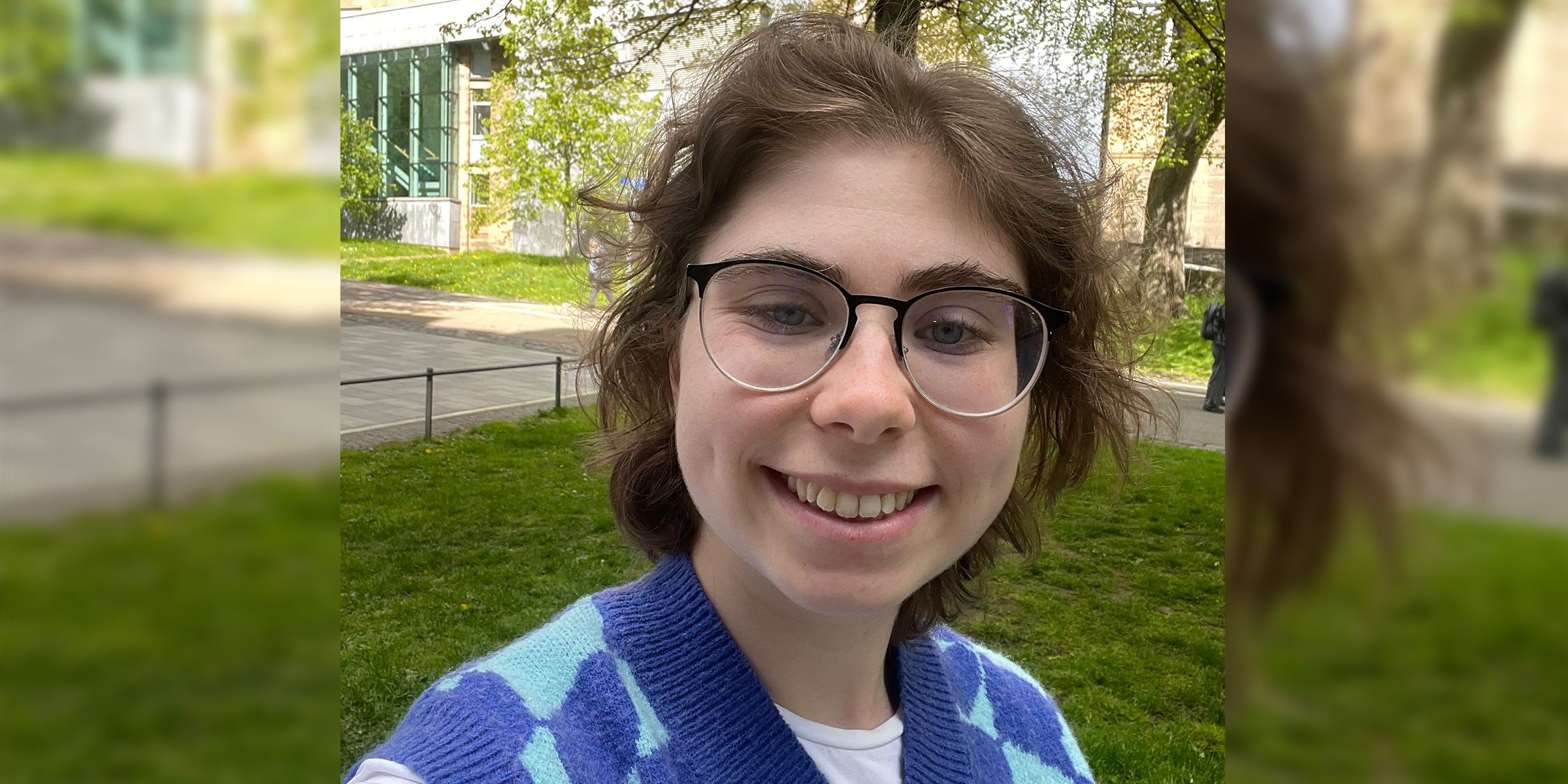 Selfie of student Emma. Emma wears glasses and a mixed blue sweater vest.