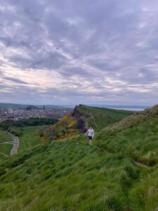 A person walks along a path on Arthur's Seat with the city of Edinburgh in the background.