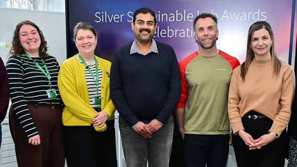 Five people stand smiling next to a screen.