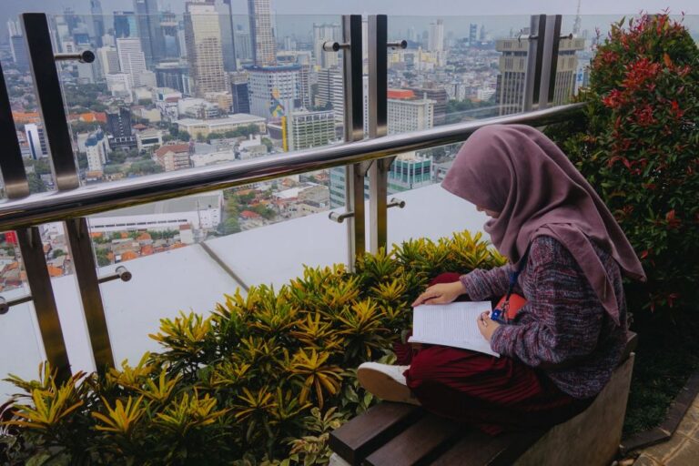 Woman sitting on bench and reading with skyline in background.