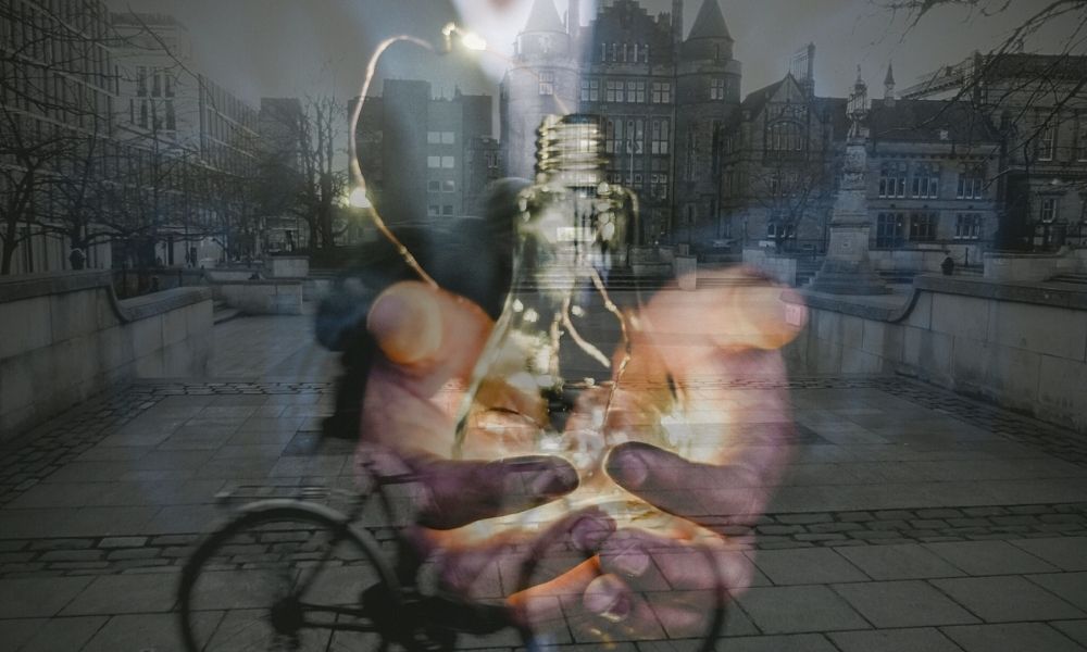 An image of hands offering a lightbulb superimposed onto a photograph of George Square at the University of Edinburgh