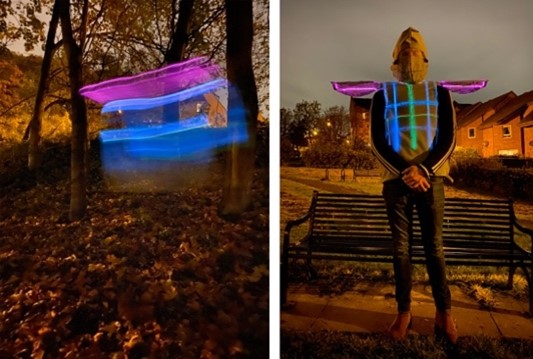 Man standing in front of a bench wearing his wearable artwork which is a rocket-suit with lED lights. 