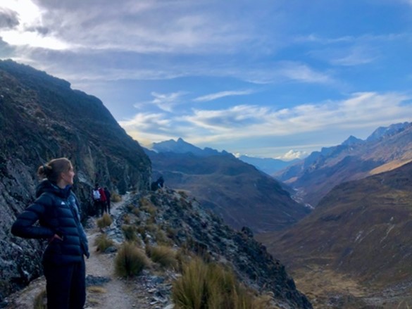 Student researcher on a mountain cliff, looking out into the mountain range.