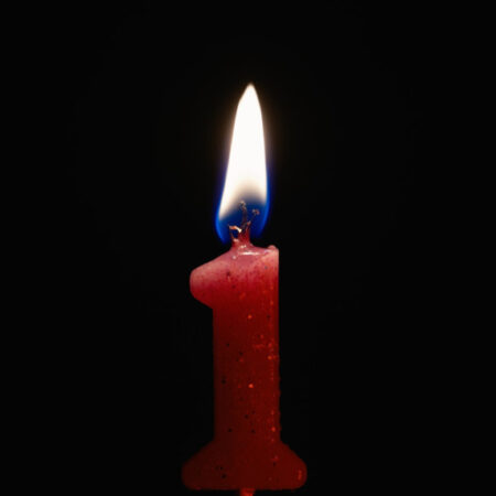 A candle in the shape of number 1 burning against a black background