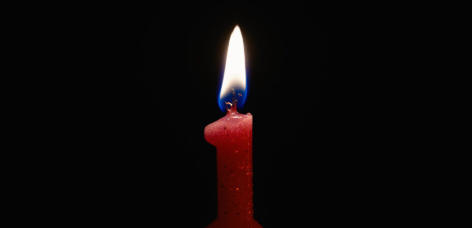 A candle in the shape of number 1 burning against a black background