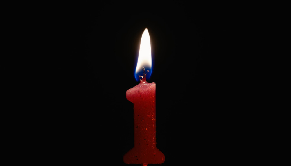 A candle in the shape of number 1 burning against a black background