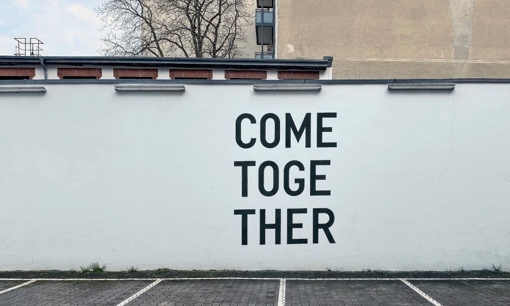 Decorative photo of tag on while wall with the words 'come together'