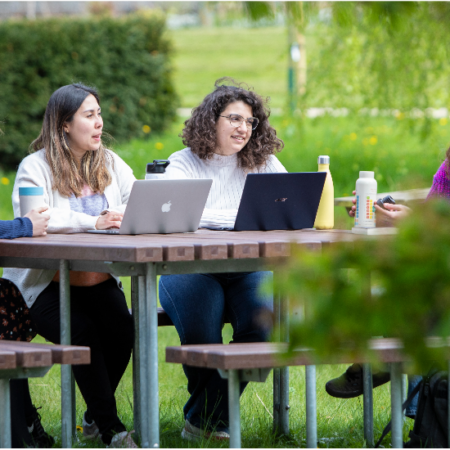 A photograph of four students sitting around a table with their desktops and chatting