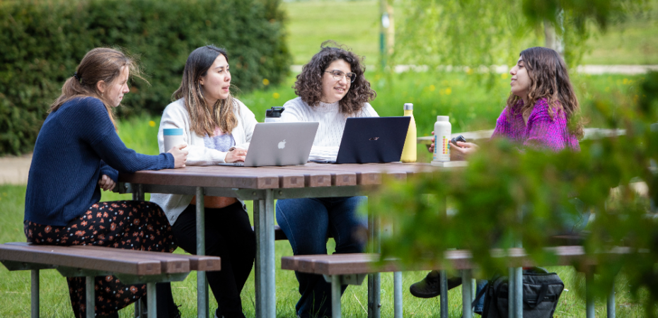 A photograph of four students sitting around a table with their desktops and chatting