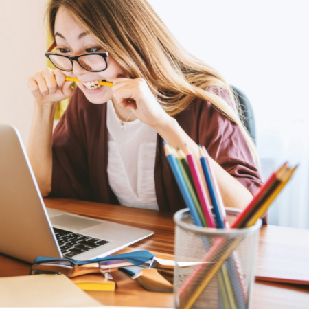 woman biting pencil while sitting on chair in front of computer during daytime