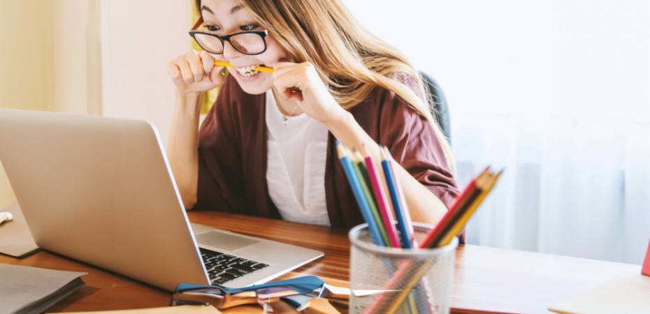 woman biting pencil while sitting on chair in front of computer during daytime