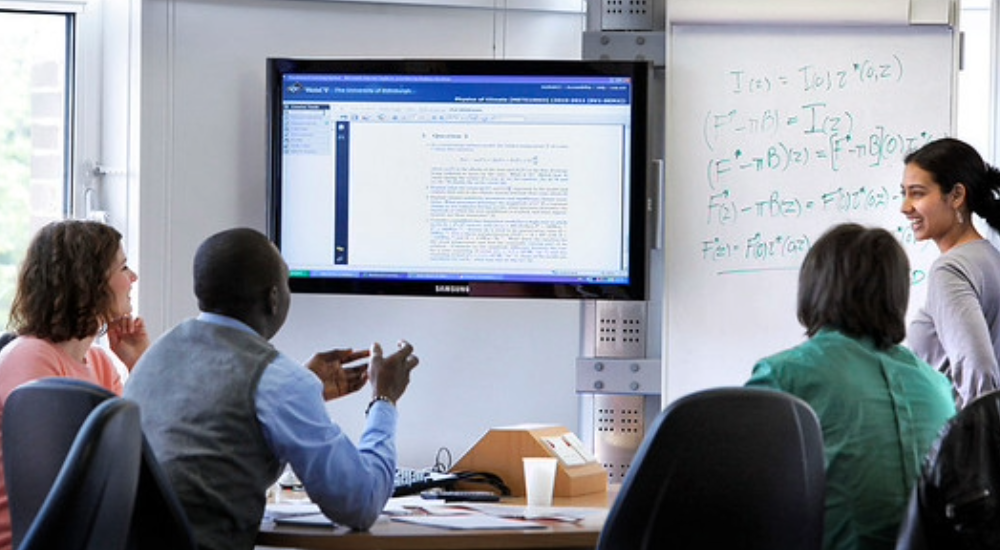 Discussion table set up, a group of people sitting around the table looking over a digital screen