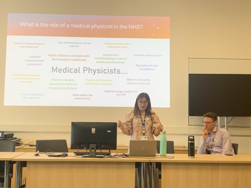 Photo of Mollie McFarlane (speaking) and Rob Williams (seated) from NHS medical physics, who spoke about the NHS medical physics training scheme.