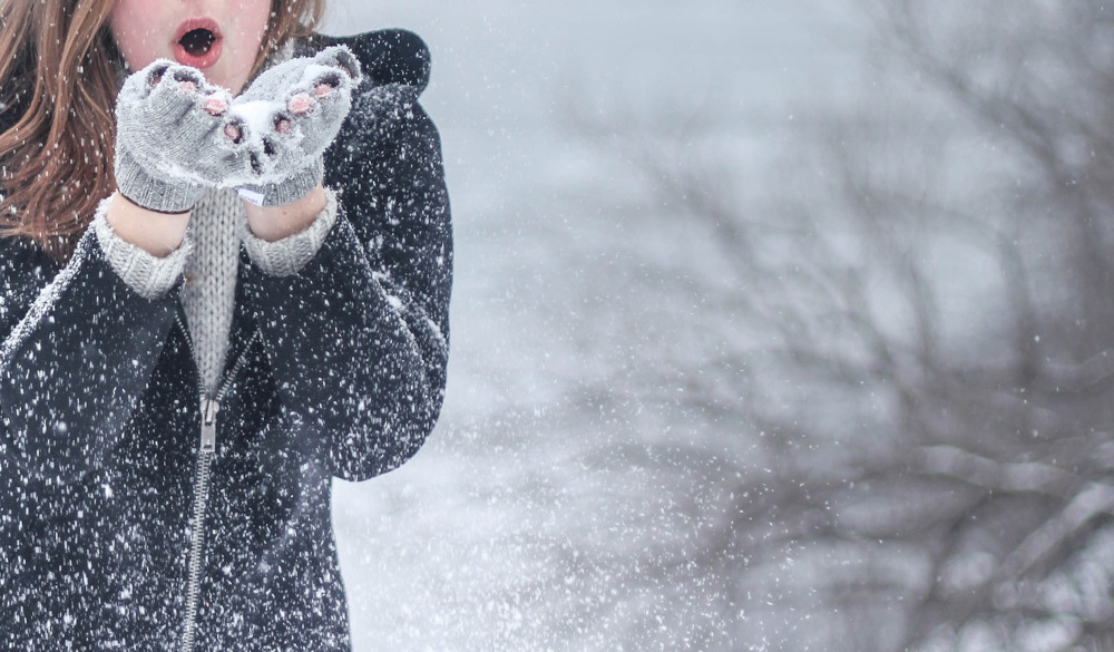 Photo of lady blowing snow out of her hands with snowy backdrop