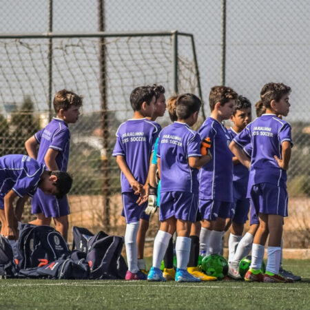 Photo of young boys playing football and talking to their coach in front of a goal.