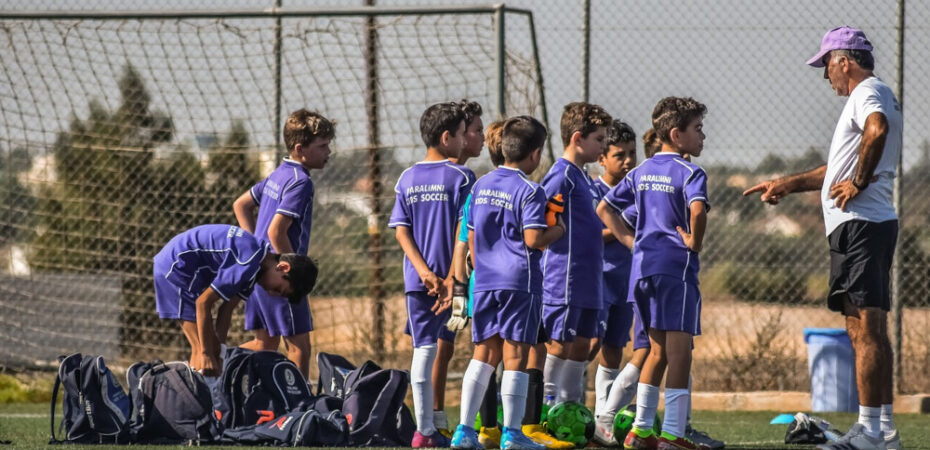 Photo of young boys playing football and talking to their coach in front of a goal.