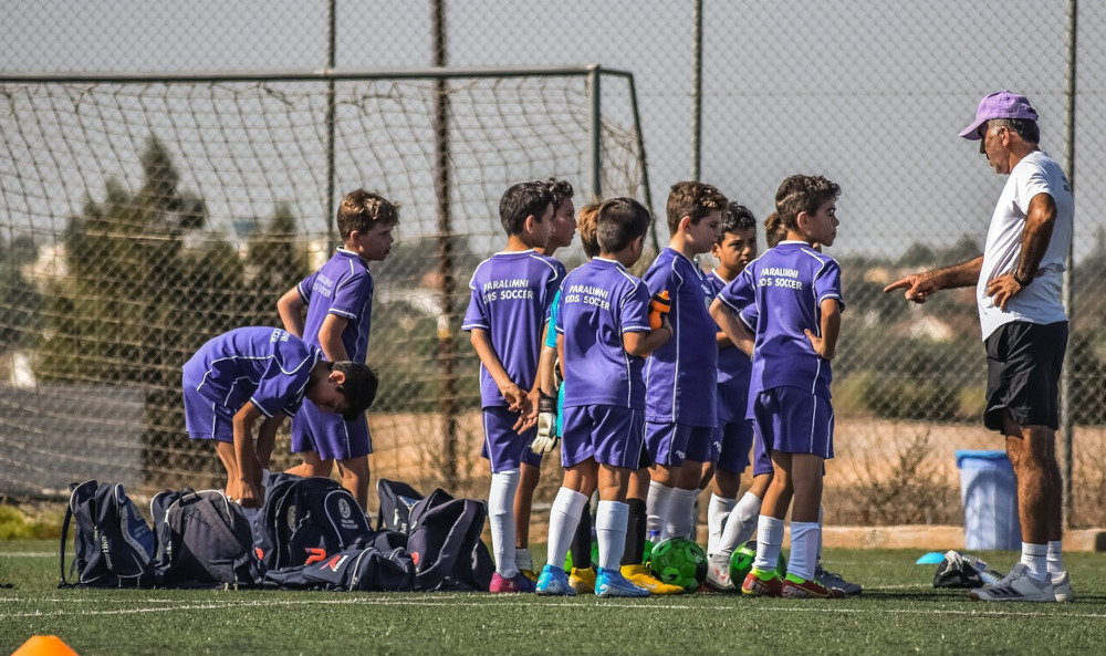 Photo of young boys playing football and talking to their coach in front of a goal.