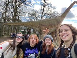 Photo of 4 students in front of a dinosaur at the zoo