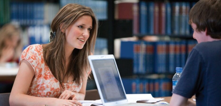Two people studying over books and laptop in library