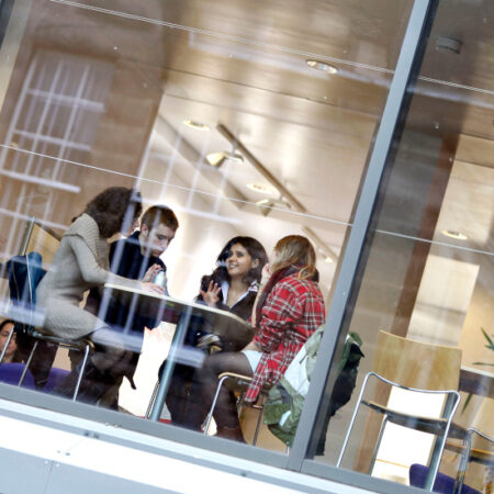 Photo of students sitting around a table in a cafe viewed through a window