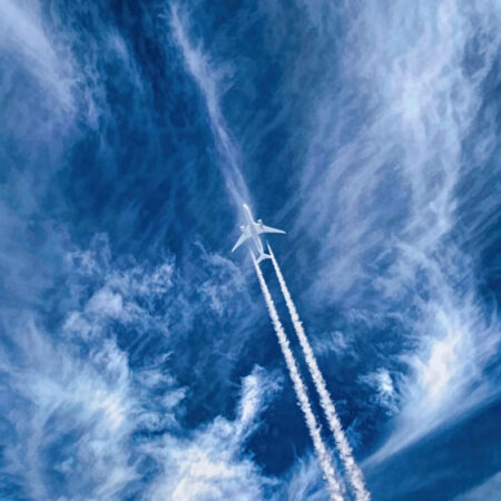Photo of a plane in sky with trails and clouds