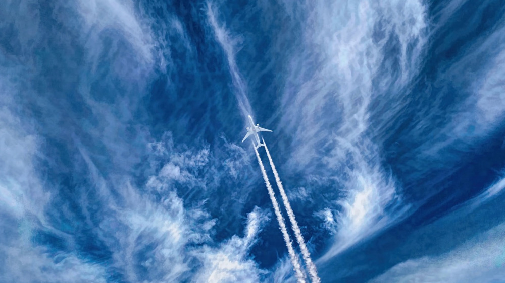 Photo of a plane in sky with trails and clouds