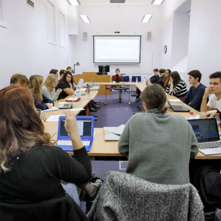 Group of students sitting around large square of desks in classroom