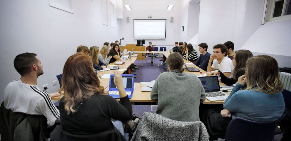 Group of students sitting around large square of desks in classroom
