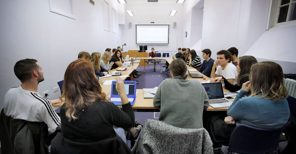 Group of students sitting around large square of desks in classroom