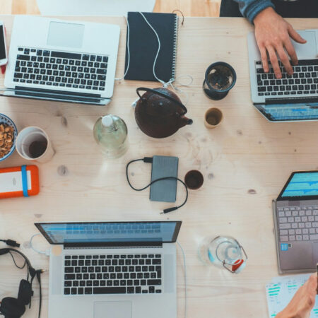 Photo of desk covered with coffee cups, laptops and tablets.