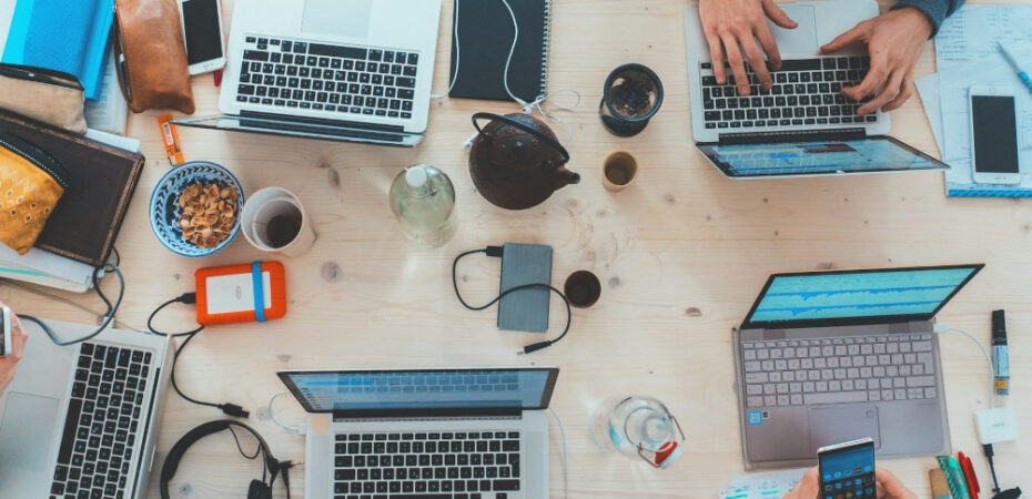 Photo of desk covered with coffee cups, laptops and tablets.
