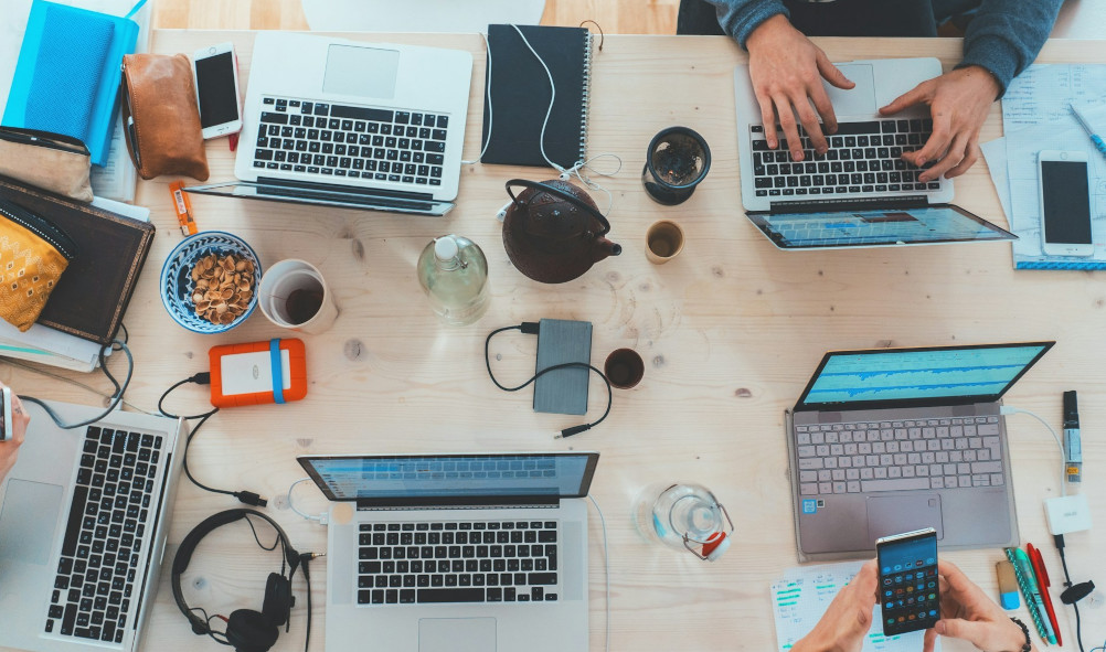 Photo of desk covered with coffee cups, laptops and tablets.