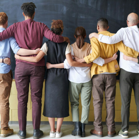 Student and staff linking arms facing blackboard