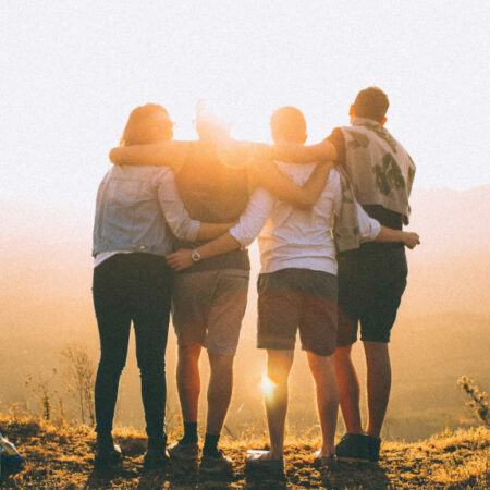 Group facing sunset on hill with arms around each other