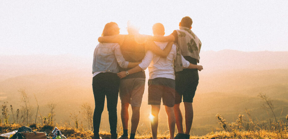 Group facing sunset on hill with arms around each other