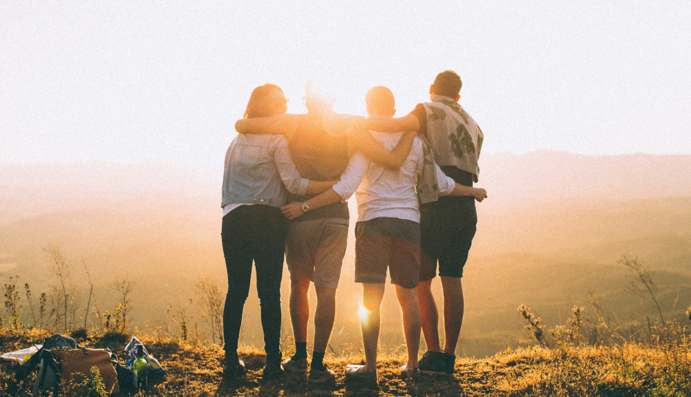 Group facing sunset on hill with arms around each other