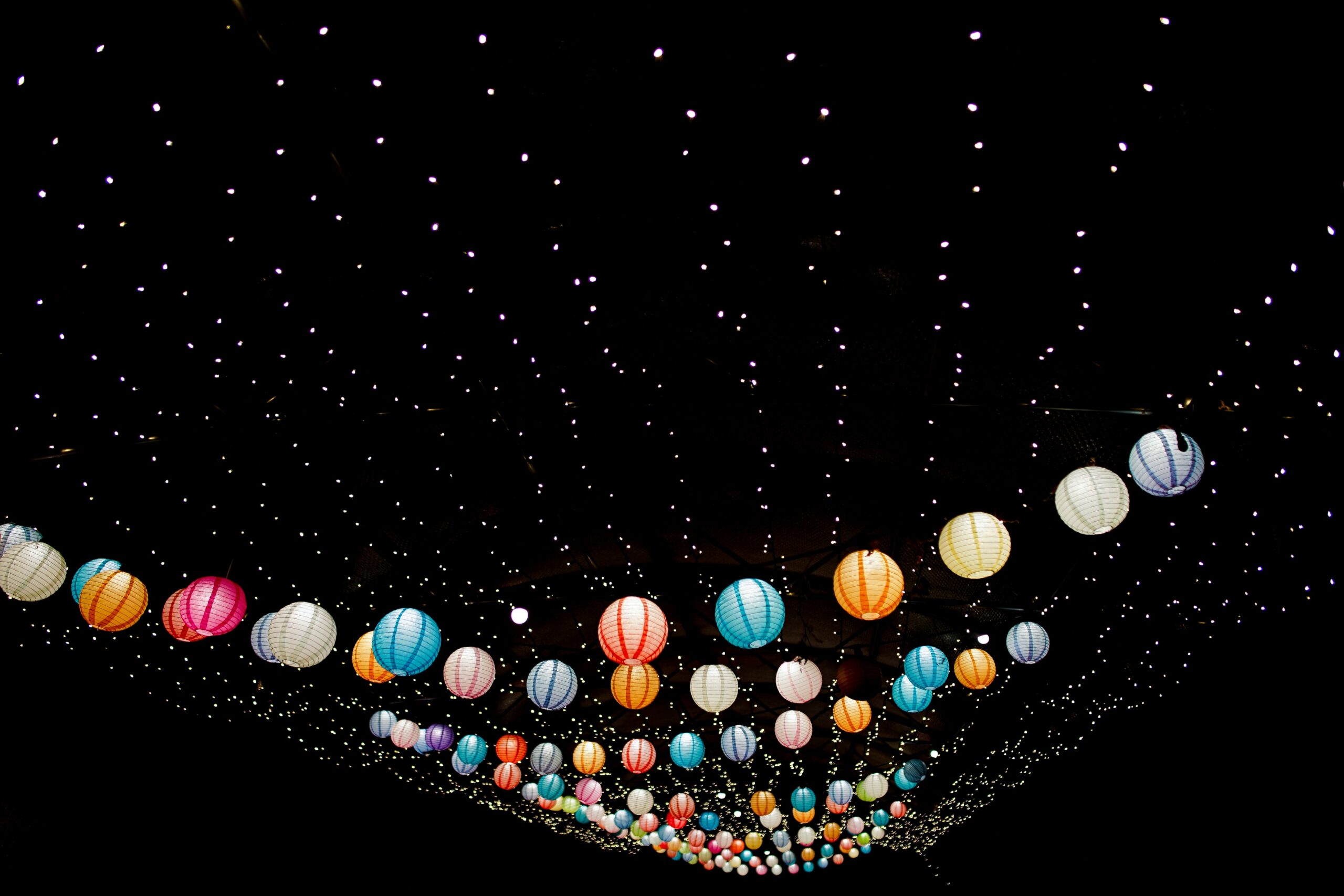 Strings of coloured, spherical lanterns against black sky.