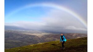 Student standing on hill with rainbow