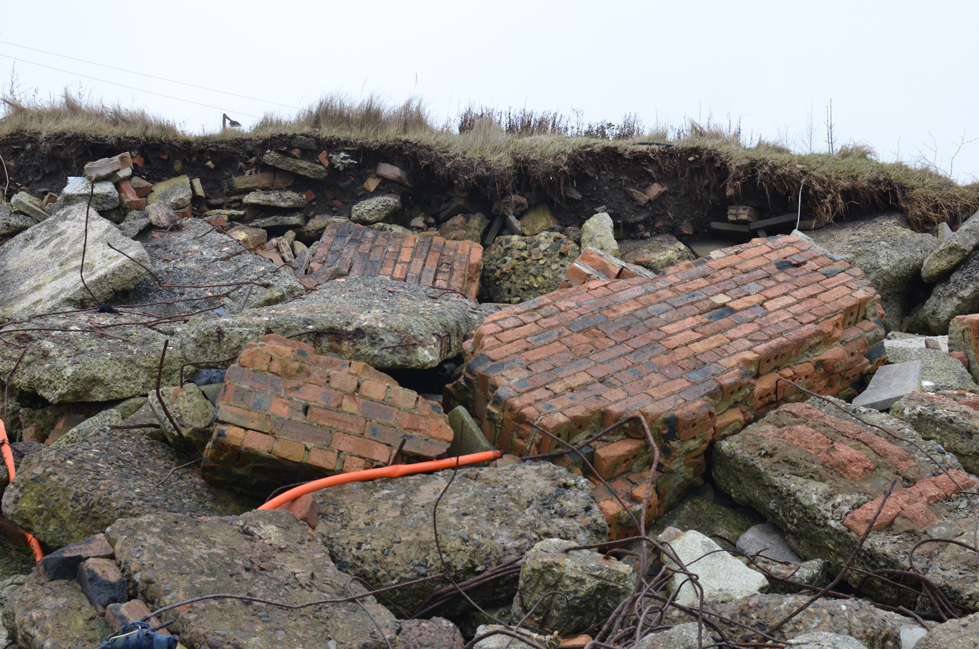 Demolition rubble dumped at Royston Beach, Granton, falls out of a cliff of soil in the background. The rubble comprises large chunks of brick walls, steel rebar and orange plastic tubing.